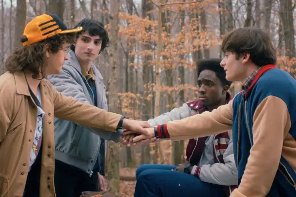 Czterech przyjaciół z Stranger Things w lesie, łączących dłonie.