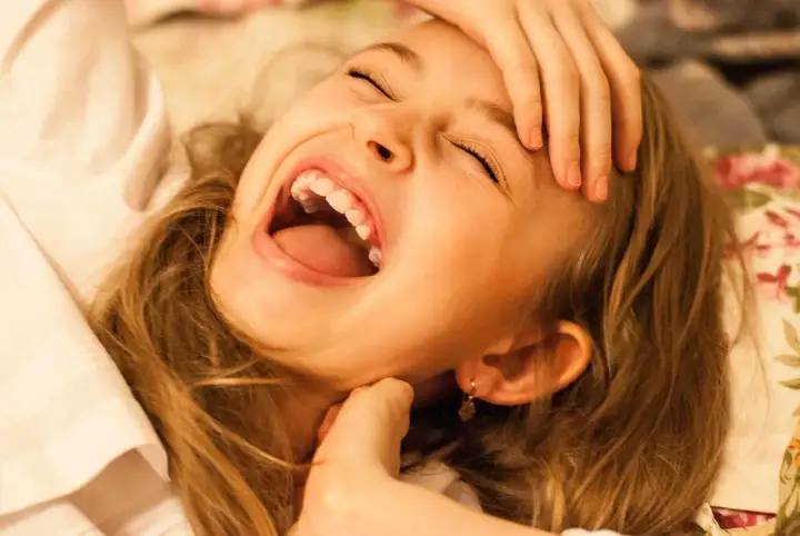Dziewczynka śmieje się tak mocno, że aż zamyka oczy. Jej usta są szeroko otwarte, a ręka podtrzymuje czoło. Śmiechom nie było końca!